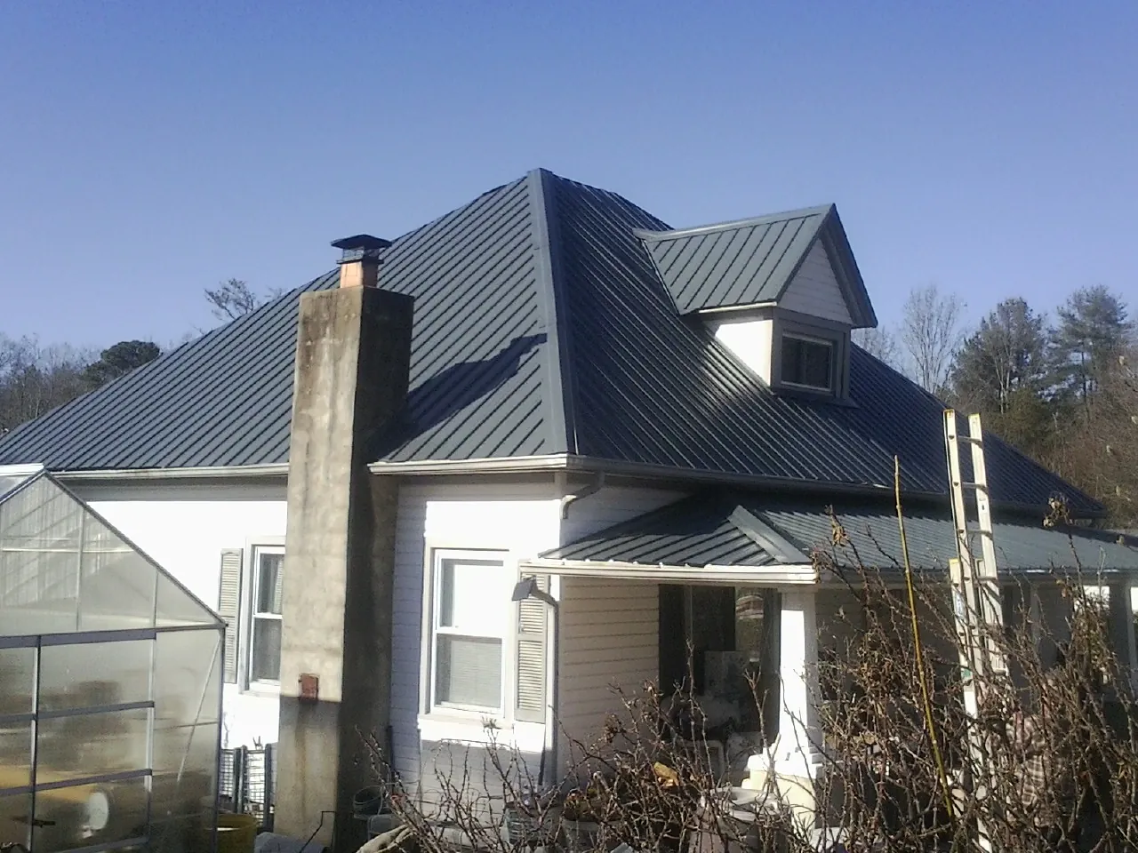 Dark blue standing seam metal roof on a white farmhouse with dormer — Slate & Tile Roof Repair by Roofing Brothers in Macksburg