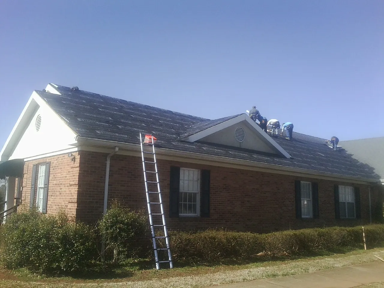 Crew tearing shingles off a brick ranch roof with a ladder set — Metal Roof Repair work by our crew in Macksburg