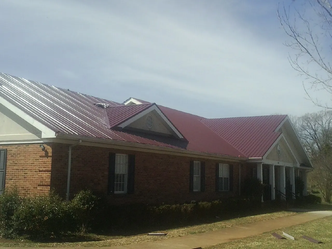 Red metal roof with gabled entries on a long brick building, from a Hail Damage Roof Repair job in Macksburg