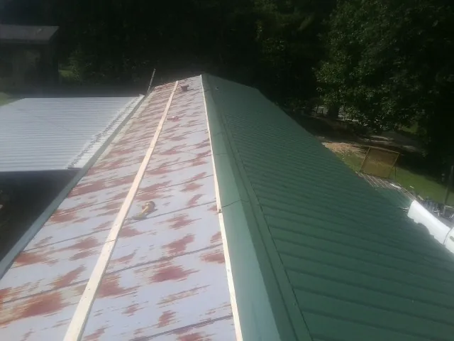 Old rusted panels beside newly installed green metal roofing — Wind Damage Roof Repair by Roofing Brothers in Macksburg