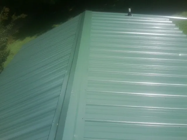 New green metal panels meeting at the ridge of a roof — Flat Roof Repair work by our crew in Macksburg