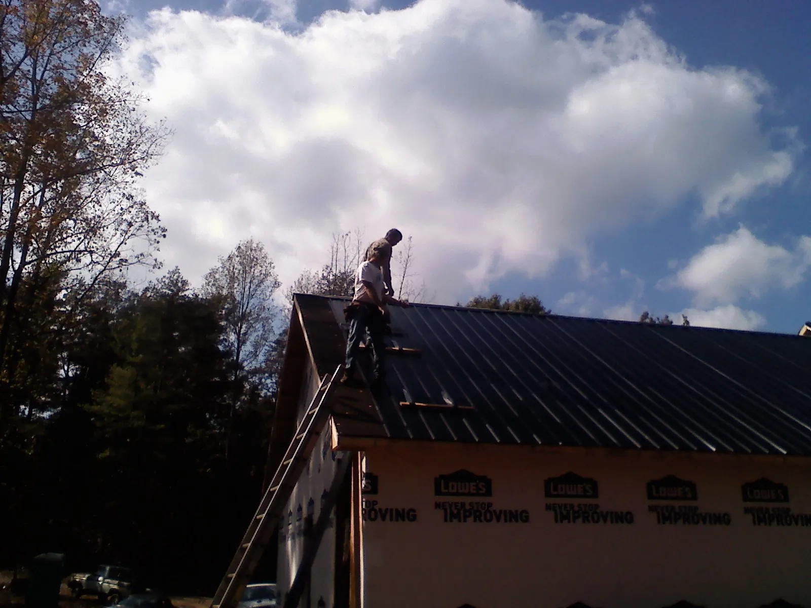 Roofer fastening dark metal panels high against a cloudy sky in Macksburg