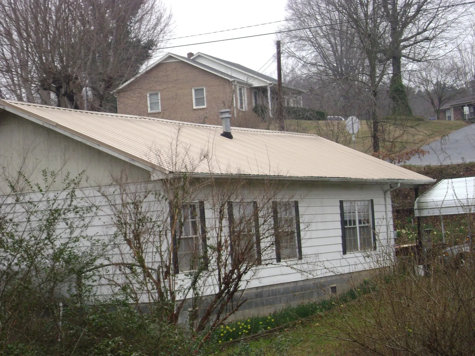 Tan metal roof on a white sided house set into a hillside — Commercial Roofing by Roofing Brothers in Macksburg